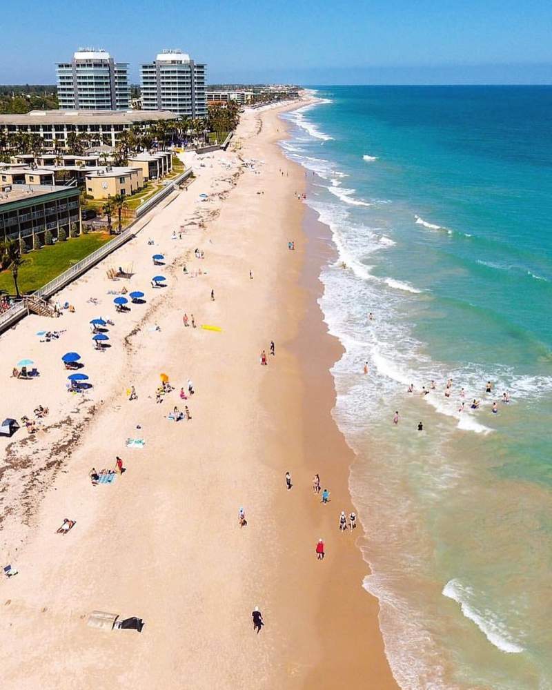 a group of people on a beach with the ocean and buildings in the background